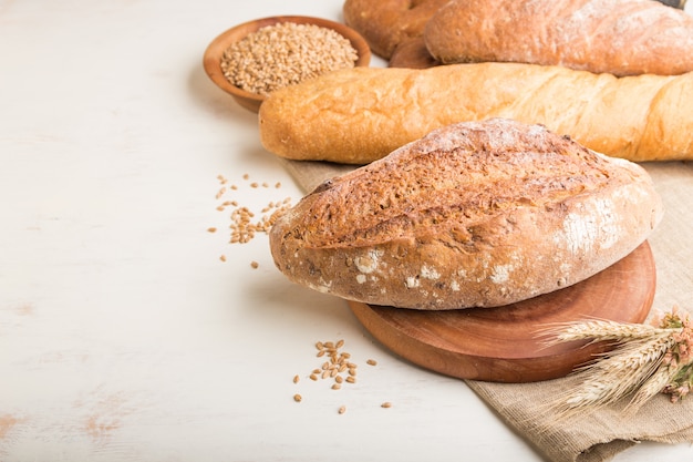 Different kinds of fresh baked bread on a white wooden surface. side view, copy space.