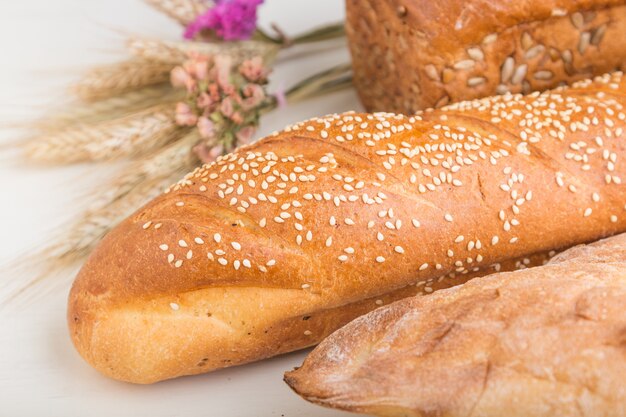 Different kinds of fresh baked bread on a white wooden surface. side view.