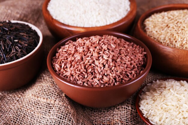 Different kinds of rice in bowls on sackcloth background