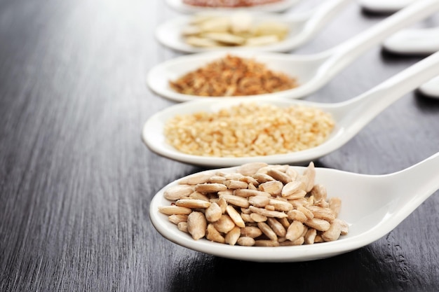 Different kinds of seeds in spoons on wooden table