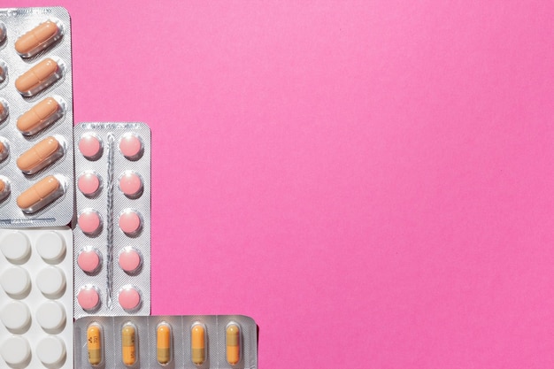 Different medicines, tablets, pills in blister pack, medications drugs on pink background. Close-up