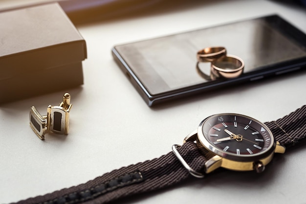 Different men's accessories such as cufflinks watches rings and phone are on the table