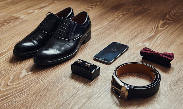 Different men's accessories such as shoes belt bow tie cufflinks and telephone are on the table