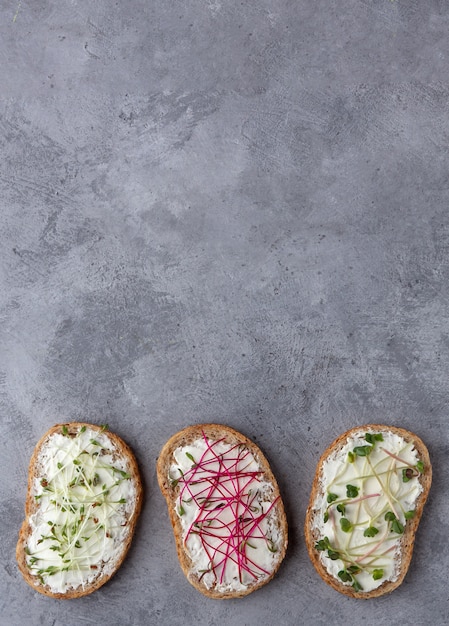 Different microgreens on sandwiches with grain bread on a concrete background