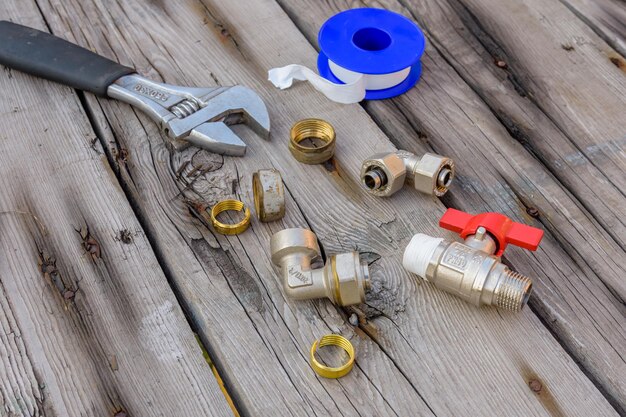 Different plumbing spare parts sealing tape and adjustable wrench on a wooden background