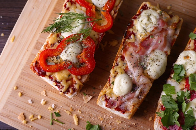 Different sandwiches with vegetables and cheese on cutting board close up