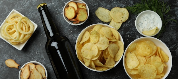 Different snacks and bottle of beer on black smokey surface