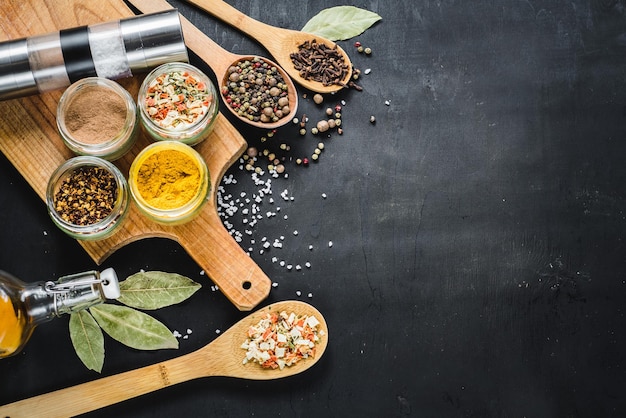 Different spices in glass and food ingredients scattered on black background