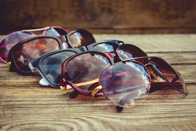 Different sunglasses on wooden background. Reflection of clouds and trees in sunglasses.