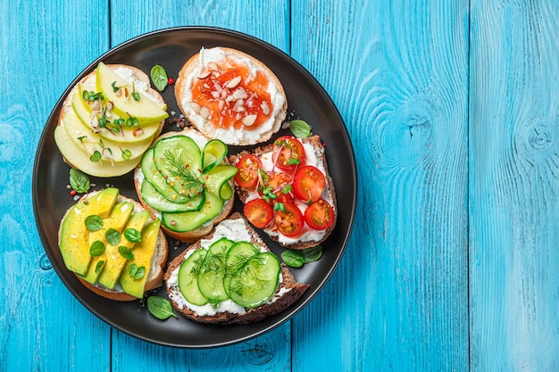 Photo different types of bruschetta with feta cheese and ricotta on a blue background