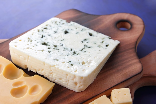 Different types of cheeses on a blue background closeup Blue cheese and yellow hard cheese on wooden boards