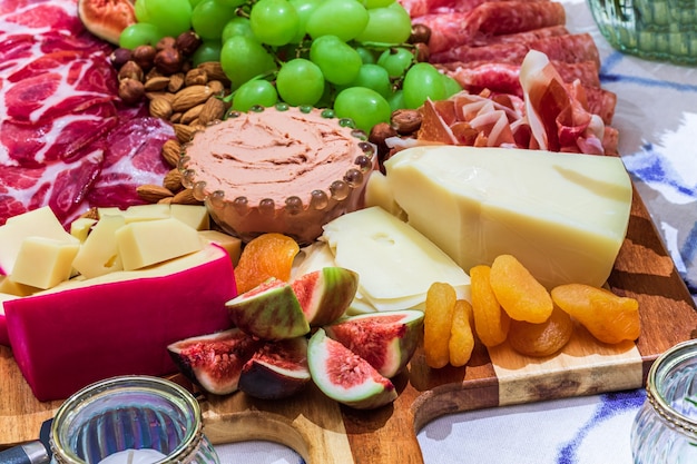 Different types of cheeses, wines, baguettes, fruits and snacks on the table for tasting and holiday scenery.