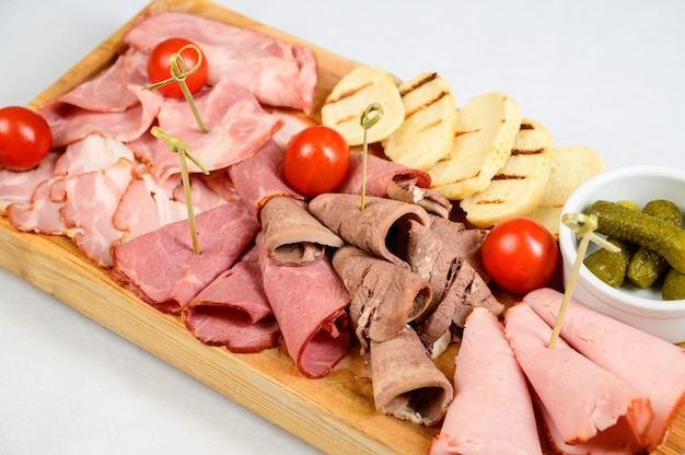 Different types of chopped sausages on a wooden board on white background