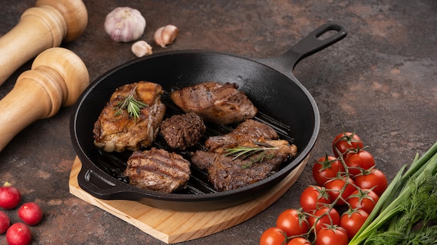 The different types of fried steak in frying pan close up view the different types of fried meat vegetables herbs spices tomato garlic pepper salt dark background high quality photo