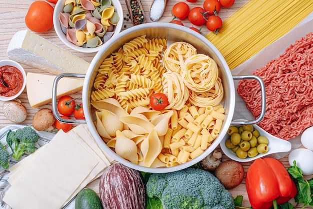 Different types of italian pasta on a wooden background with various ingredients for cooking traditional italian dishes