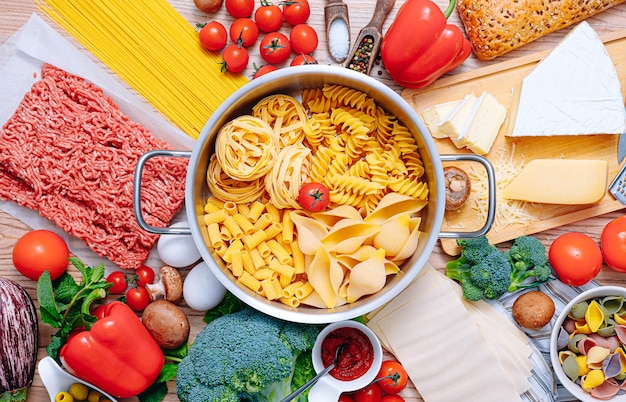 Different types of italian pasta on a wooden background with various ingredients for cooking traditional italian dishes