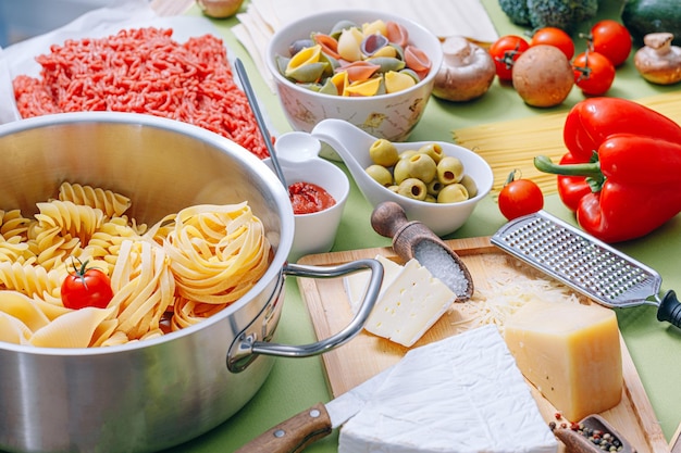 Different types of italian pasta on a wooden background with various ingredients for cooking traditional italian dishes