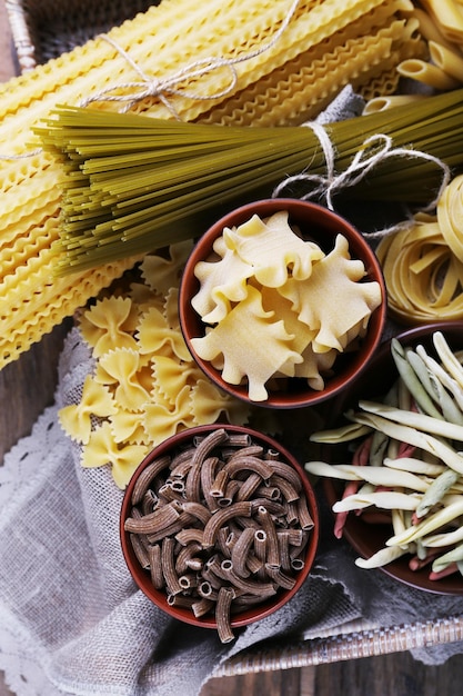 Different types of pasta in wicker basket with fabric on rustic wooden table background