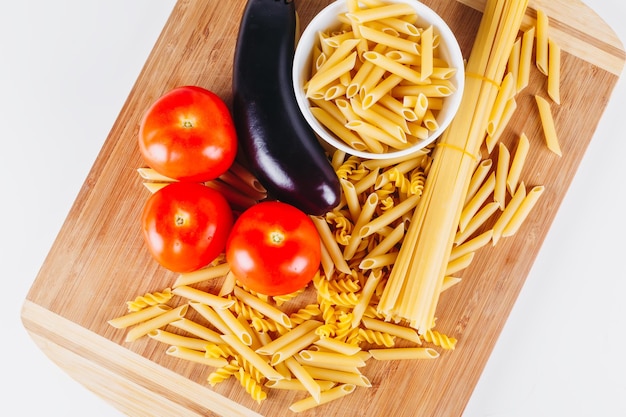 Different types of raw italian pasta with tomatoes and other vegetables top view background selected