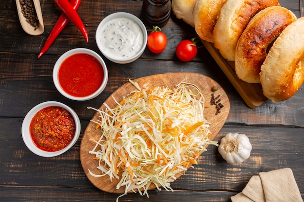 Different types of sauces in bowls on cutting Board with garlic and shredded cabbage and tortillas. On dark rustic