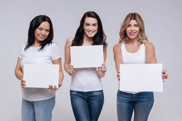 Different but united. Spectacular active strong ladies holding up white signs while posing and wearing simple clothes