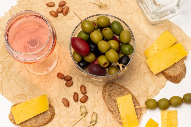 Different varieties of olives in a glass bowl Glass of rose wine bread with cheese on paper