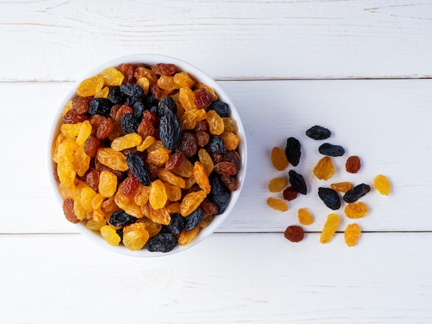 Different varieties of raisins in a bowl on a white wooden background Top view