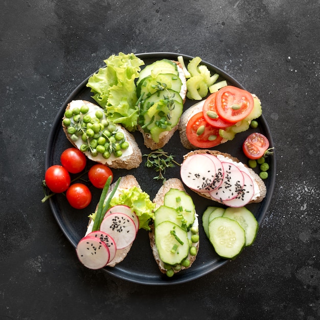 Different vegan sandwiches with vegetables, radish, tomato, rye bread on black. Appetizer for party.