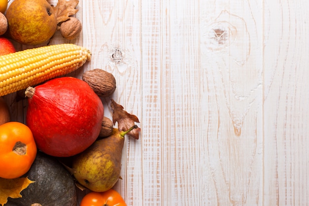 Different vegetables pumpkins, apples, pears, nuts, corn, tomatoes, dry yellow leaves on white wooden background. Autumn Harvest , copyspace.