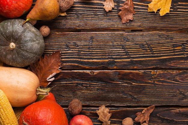 Different vegetables, pumpkins, apples, pears, nuts, tomatoes, corn, dry yellow leaves on wooden background. Autumn mood, copyspace. Harvest .