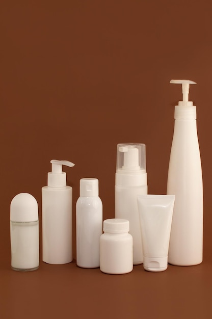 Different white bottles and tubes for cosmetics on a brown background with space for text