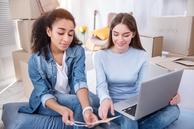 Difficult choice. Pleasant young women sitting on the floor in their new apartment and choosing the color for the walls