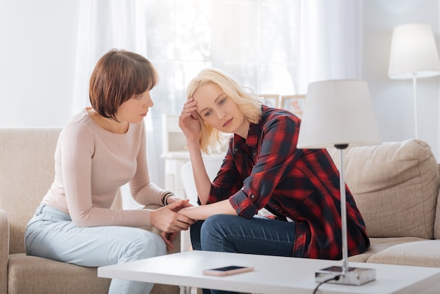 Difficult times. Depressed cheerless blonde woman sitting together with her partner and holding the forehead while thinking about problems