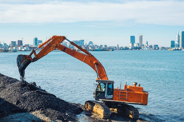 A digger is digging a hole in the water with a city in the background.