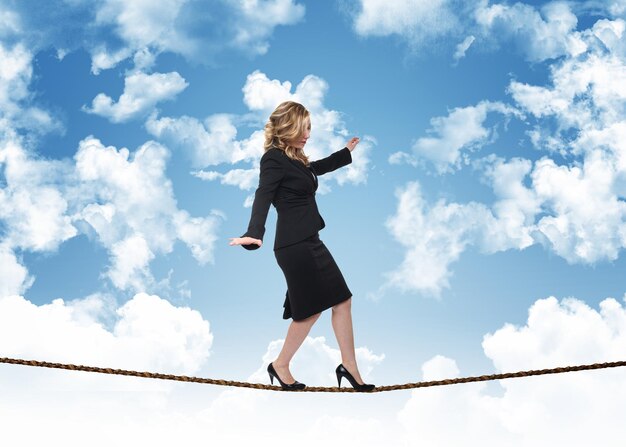 Photo digital composite image of businesswoman balancing while walking on tightrope against blue sky