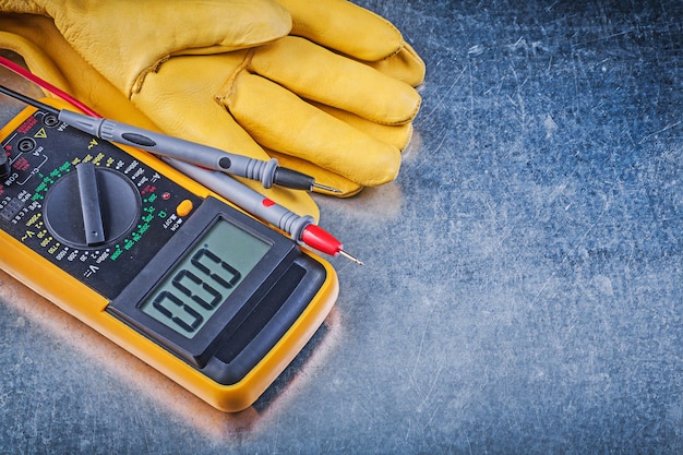 Photo digital electrical tester test leads pair of safety gloves on metallic background