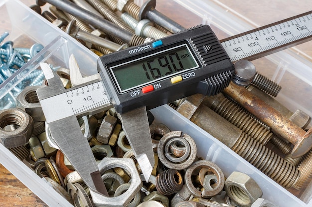 Digital electronic caliper on a background of opened storage box with rusty used bolts and nuts