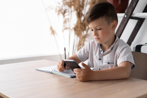 Digital generation child doing homework using a mobile phone Lessons with a gadget via the Internet A schoolboy writes tests from a smartphone Online education concept