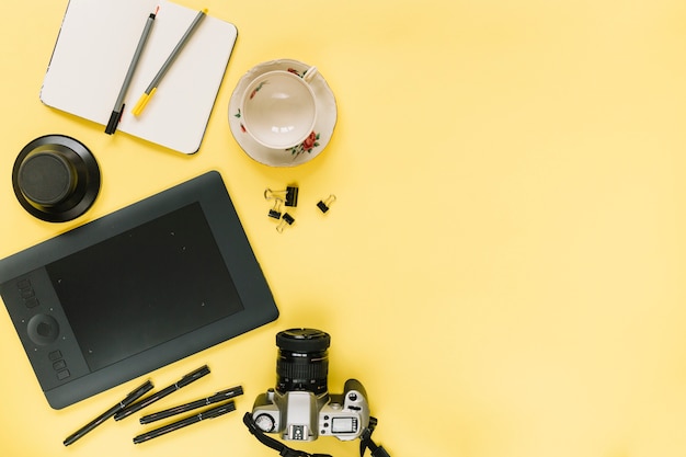 Digital graphic tablet; camera; stationery and empty cup on yellow background