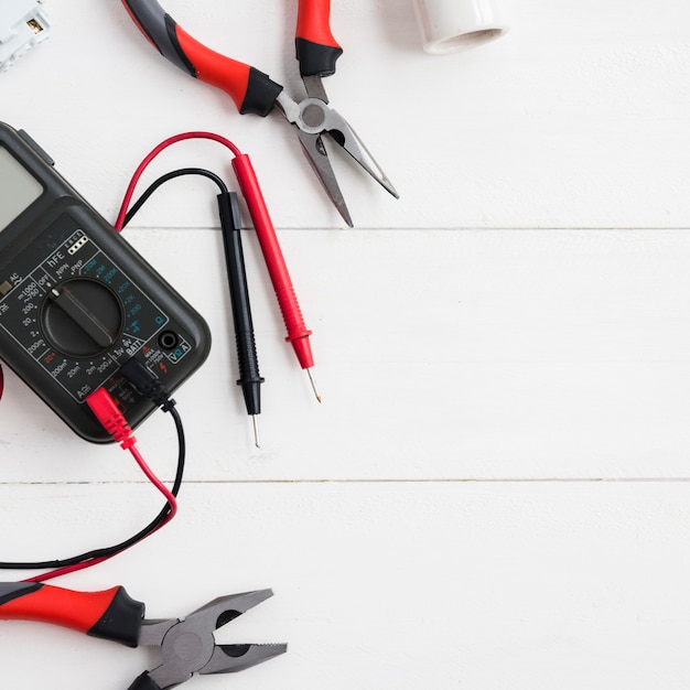 Digital multimeter with tester and pliers on white wooden table