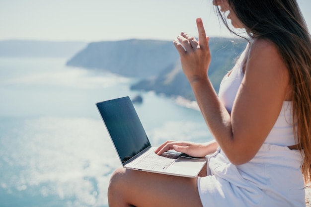 Digital nomad woman in the hat a business woman with a laptop sits on the rocks by the sea during