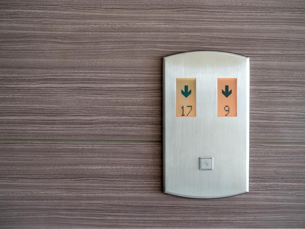 Digital number and down arrow on metallic elevator call panel on wooden pattern wall background