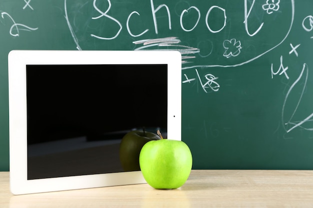 Photo digital tablet and apple on desk in front of blackboard