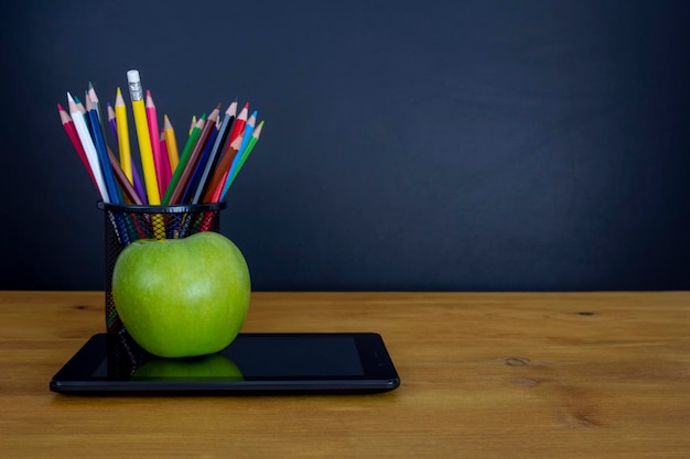 Photo digital tablet and apple on the desk in front of blackboard