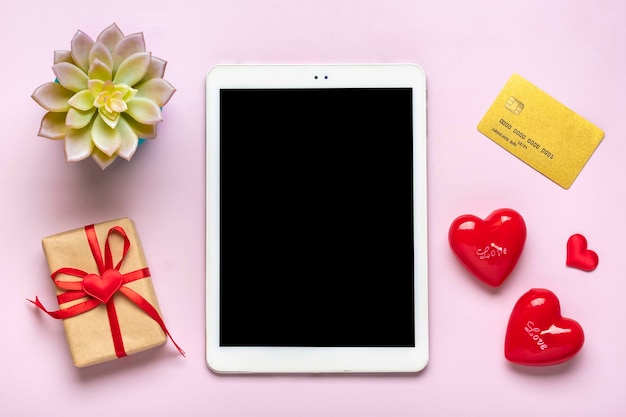 Digital tablet for chooses gifts, makes purchase, envelope, red hearts on pink table Top view Flat lay Holiday shopping list, Happy Valentine's day, party, online shop concept Mock up