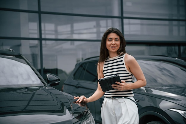 Digital tablet in hand Attractive young woman is outdoors near her brand new car