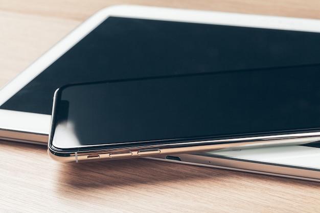 Digital tablet and mobile phone. Electronic devices on wooden table, close up.