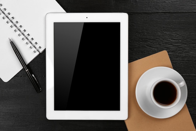 Digital tablet with cup of coffee and notebook on wooden table closeup