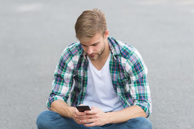 Photo digital technologies. handsome man checkered shirt. male fashion. student relax use phone. guy chatting outdoor. street style. man sit on ground. carefree student. free time spending. summer fashion.