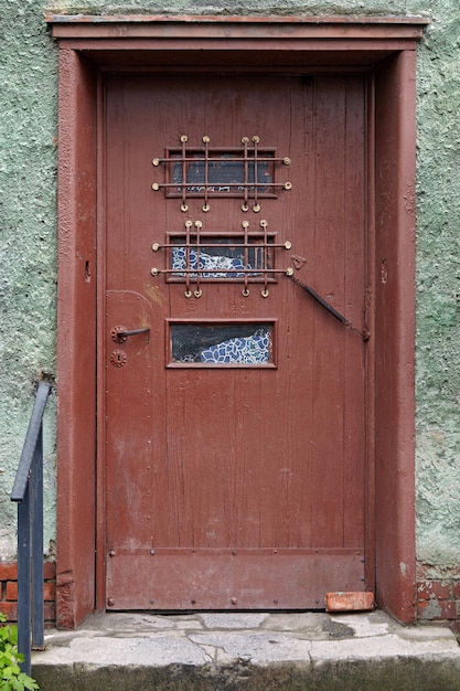 Dilapidated shabby brown wooden door on the green wall of an old house